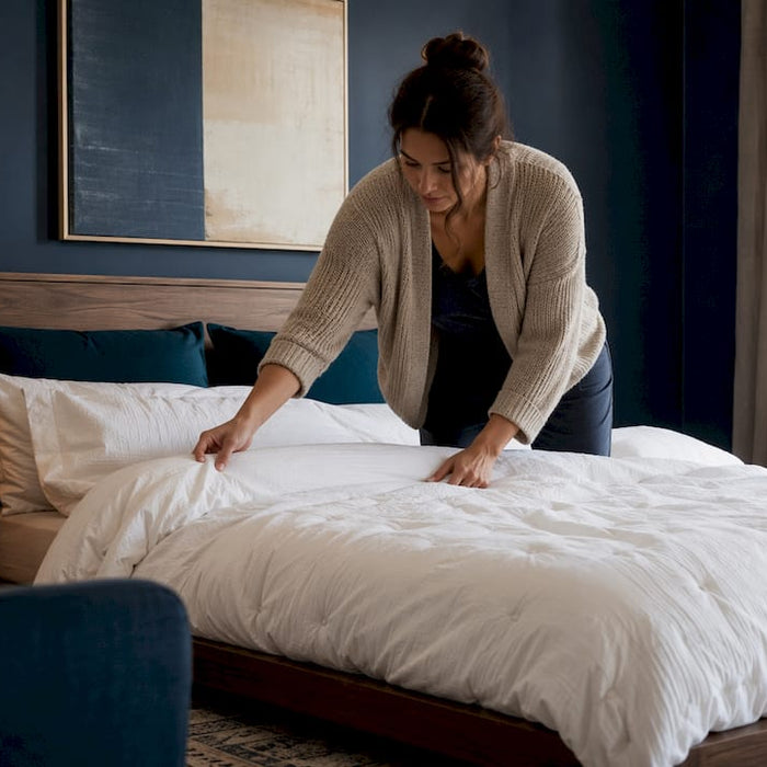Woman arranging king duvet insert on bed in bright bedroom