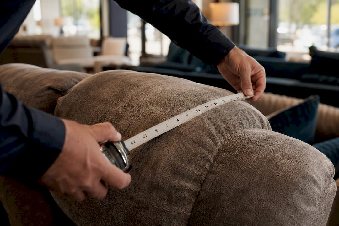 Hands measuring sofa seat depth with tape